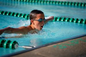 Boy wearing goggles swimming in an indoor pool.