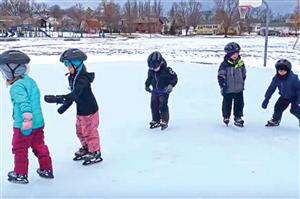A group of small children ice skating outdoors.